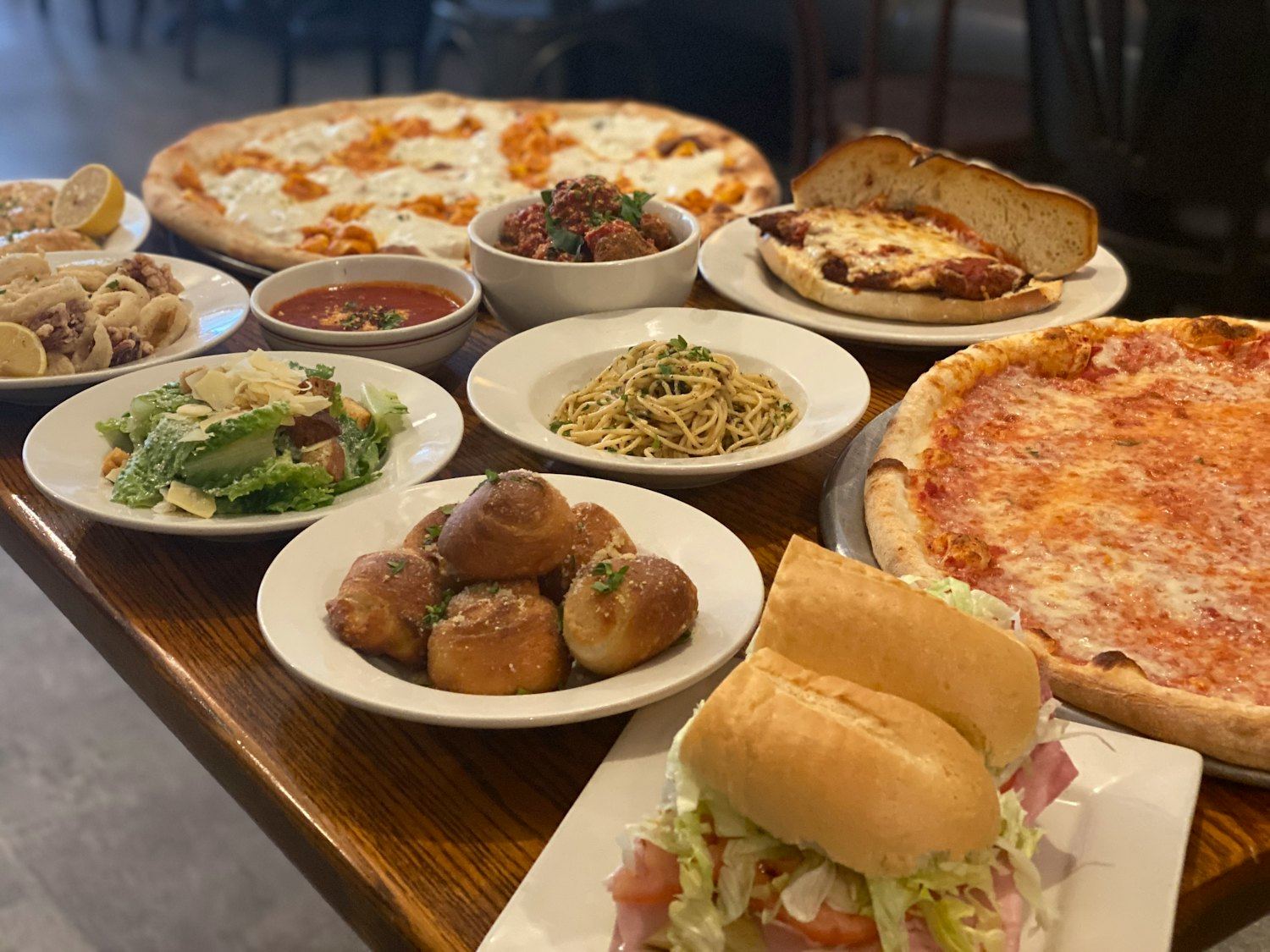 A table spread with pies, garlic knots, salads, pasta and a hero sandwich
